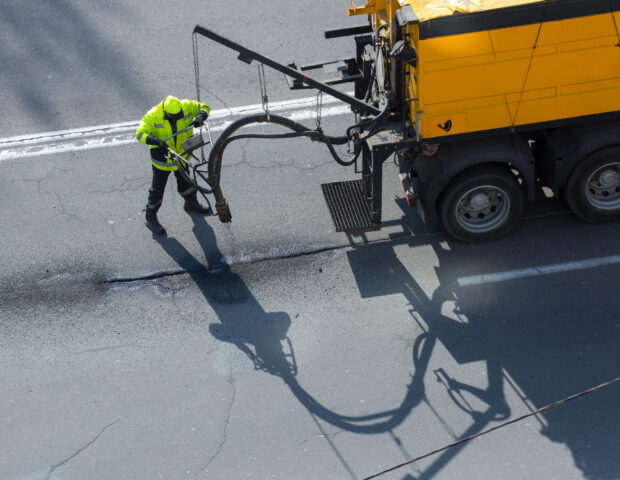 Road surface restoration work. The worker performs on road patcher work on the repair of cracks by filling and sealing with coated by bitumen emulsion and dry aggregate in the asphalt surface.