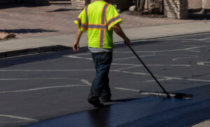 Worker using a sealcoating brush during asphalt resurfacing project